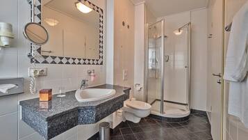 A modern bathroom with a granite countertop sink, a toilet, and a glass-enclosed shower.