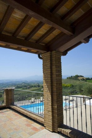 A covered outdoor area with a brick column, a pool, and a view of a hilly landscape. - Agriturismo Aqua Viva (Acquaviva Picena)