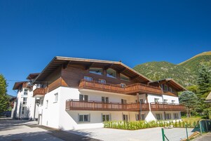 A multi-story building with balconies, a sloped roof, and a mountainous backdrop.