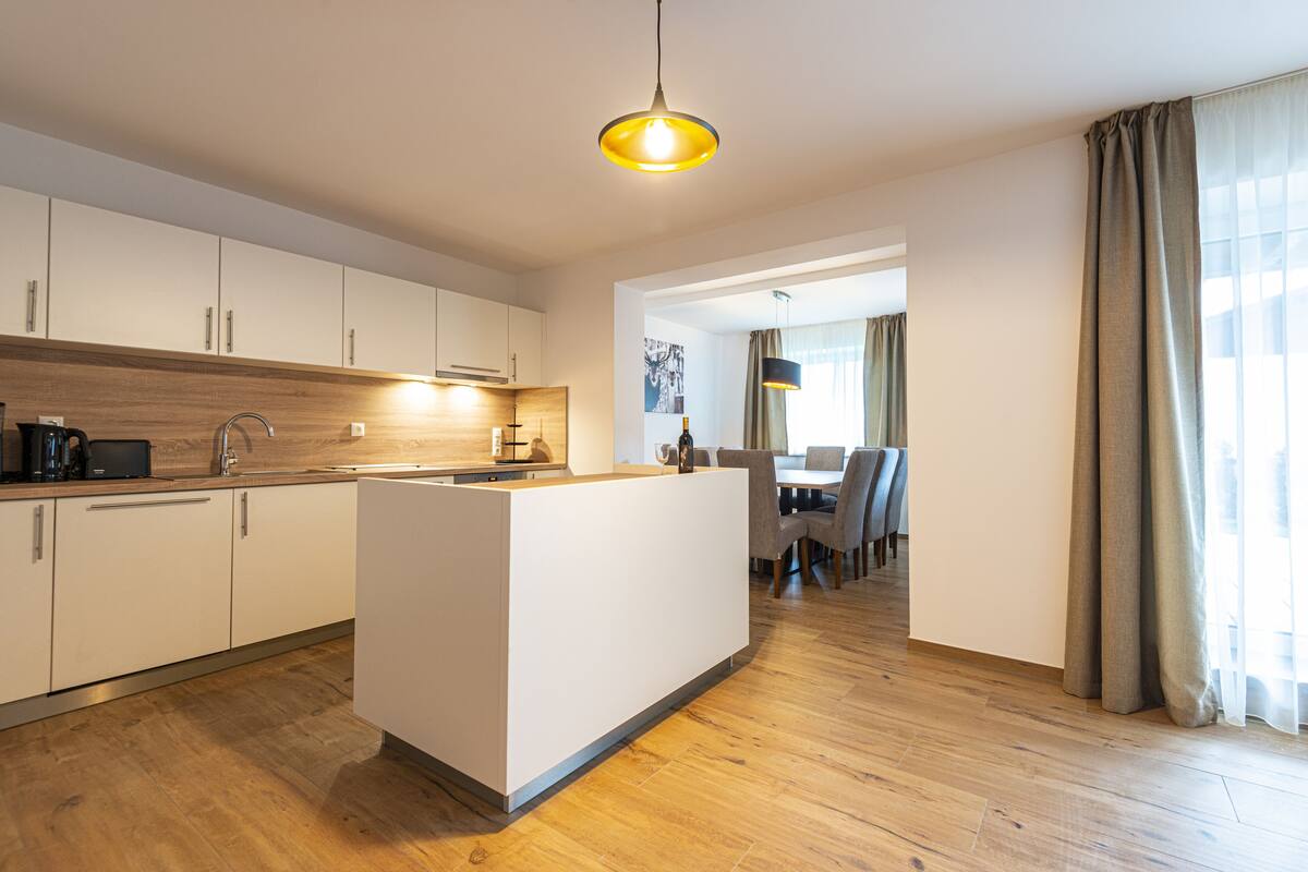 Een moderne keuken met een centraal eiland, houten vloeren en een eethoek met een tafel en stoelen.