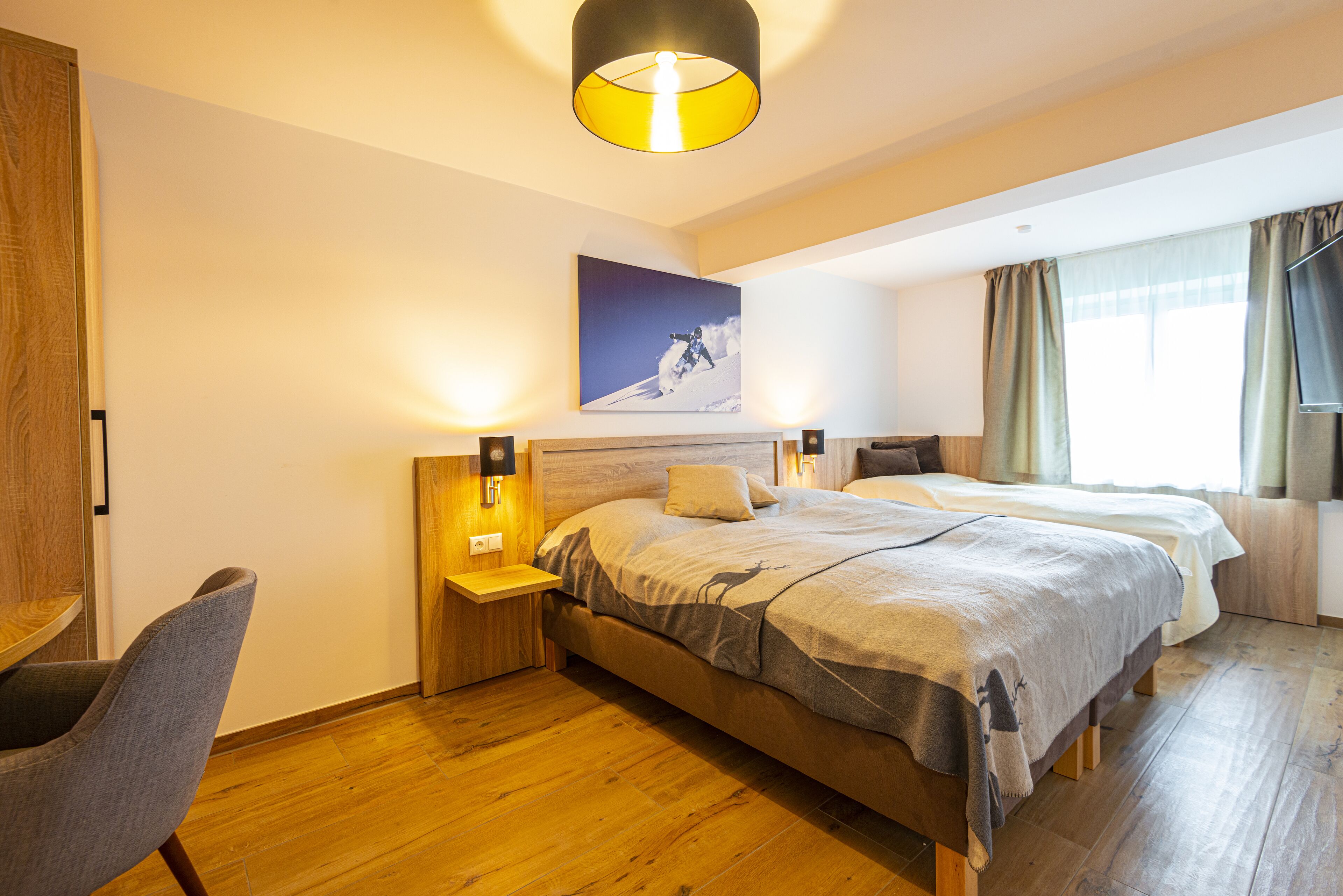 Habitación de hotel con dos camas, suelo de madera, un escritorio y una silla.