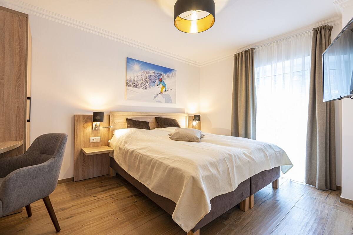 Een slaapkamer met een groot bed, een stoel, een nachtkastje en een schilderij aan de muur.