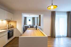 A modern kitchen with a central island, built-in oven, and a dining area with a table and chairs.