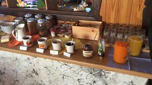 A breakfast bar with various food items and beverages, including jars of spreads, a pitcher of orange juice, and a mug with a strawberry design. - Pension Fernblick (Sankt Oswald-Riedlhuette)