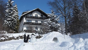 A snowman in front of a building with a balcony, surrounded by snow-covered trees. - Pension Fernblick (Sankt Oswald-Riedlhuette)