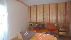 A bedroom with a wooden headboard, a bed with two pillows, a nightstand with a vase of flowers, and a wooden floor. - Pension Fernblick (Sankt Oswald-Riedlhuette)