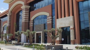 A modern building with a large glass facade, a prominent entrance with an arch, and a sign reading "MENARA MALL". - Residence La perle de l'atlas (Marrakech)