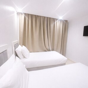 A hotel room with two beds, a headboard, a wall-mounted TV, and a window with curtains.