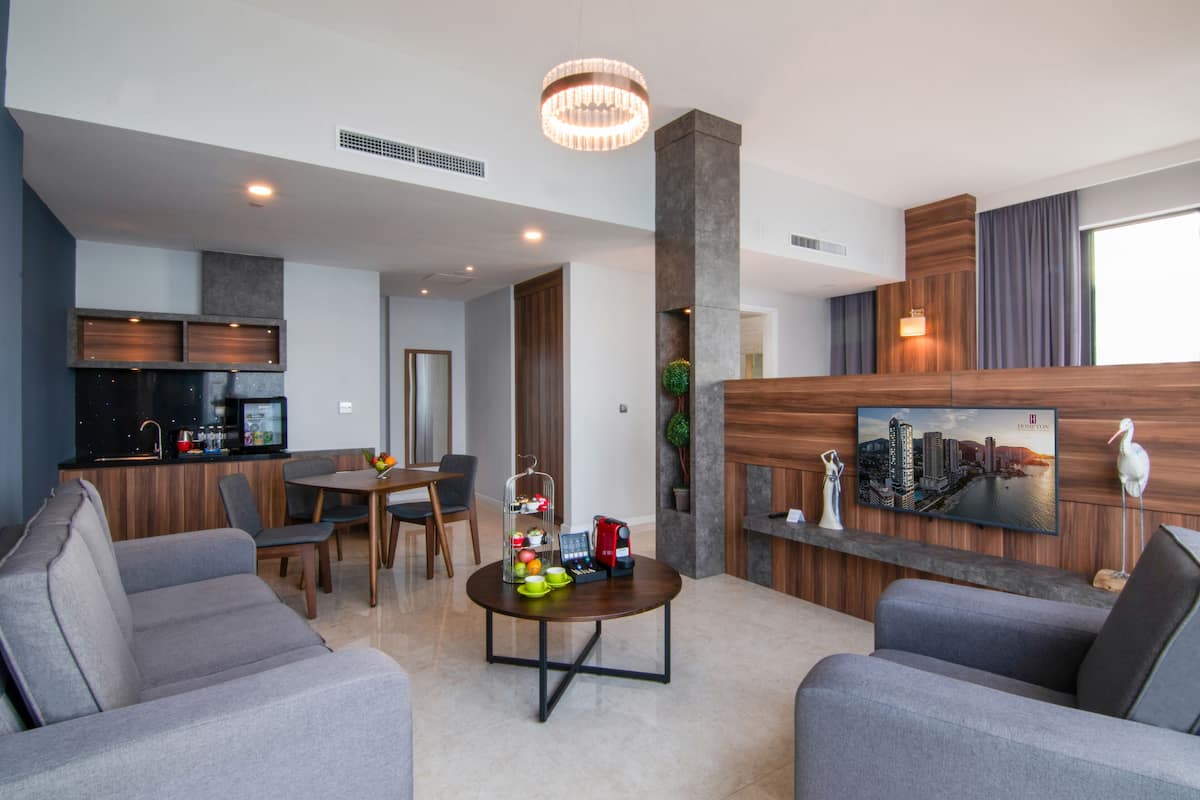 A modern living room with a dining area, a kitchen, and a large TV mounted on the wall.