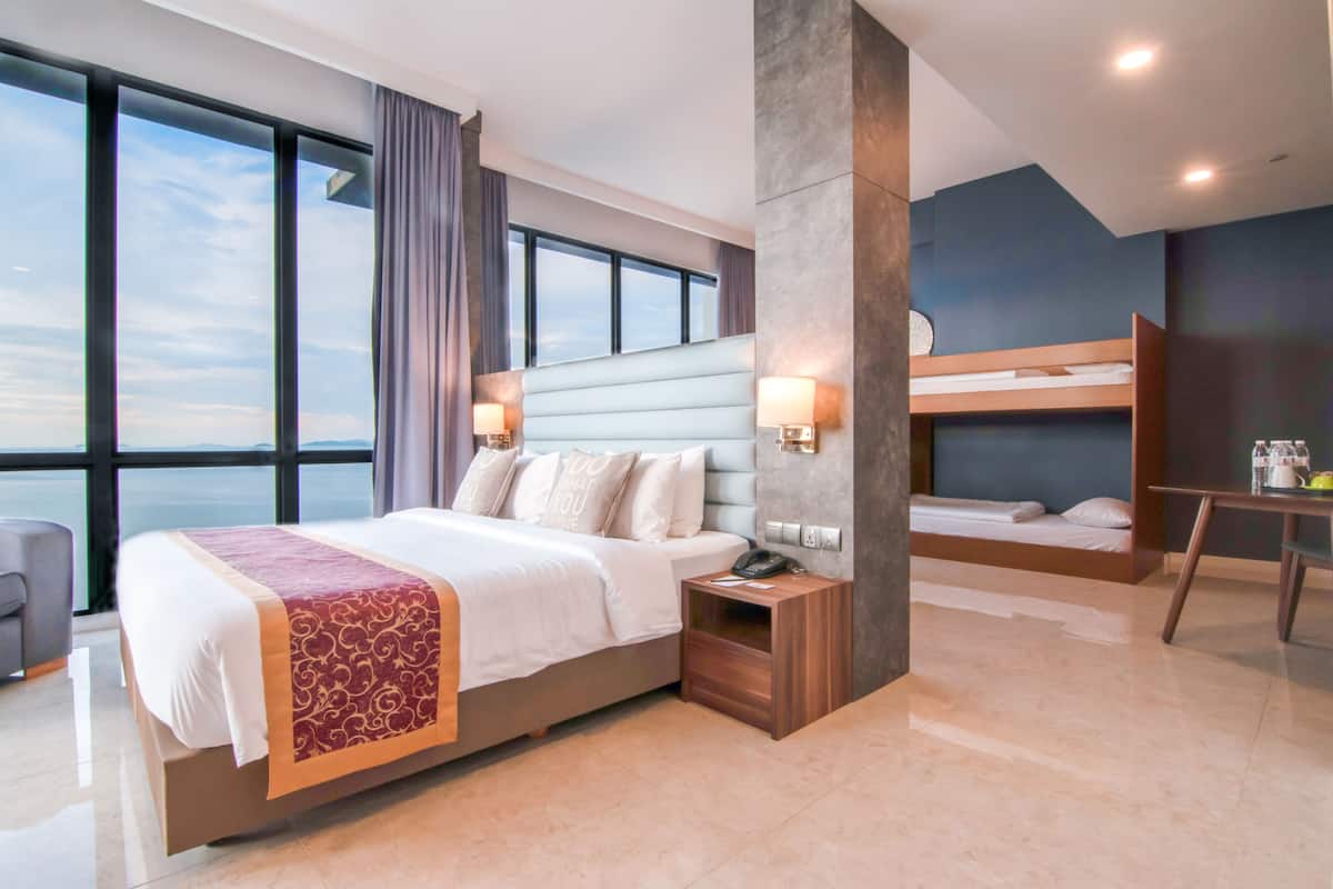 A modern hotel room with a large bed, a smaller bunk bed, a desk, and a view of the city skyline.