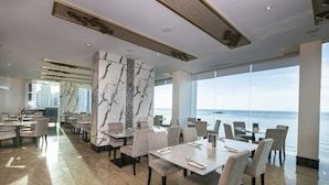 A modern dining area with marble walls, large windows, and a view of the sea. - Hompton by the Beach Penang (George Town)