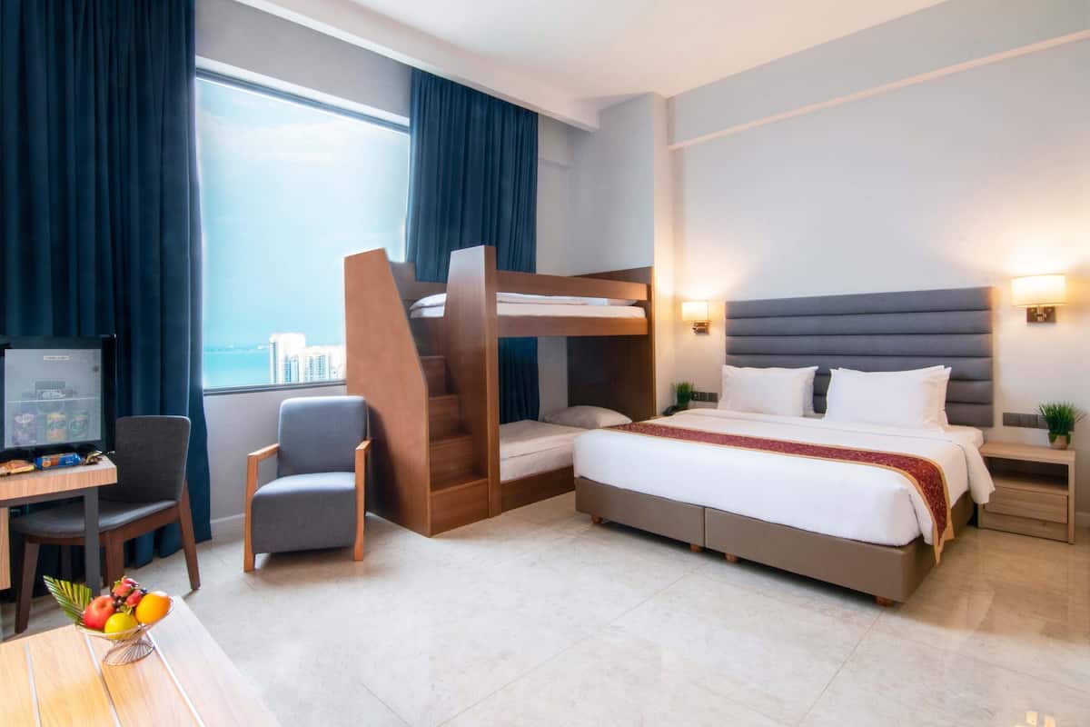 A hotel room with a bunk bed, a desk with a chair, a television, and a fruit bowl.