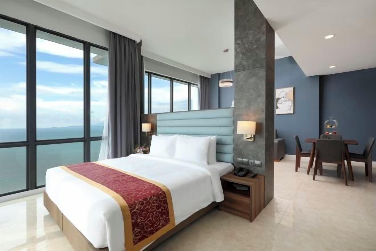 A hotel room with a large bed, a desk with a chair, and a view of the ocean.