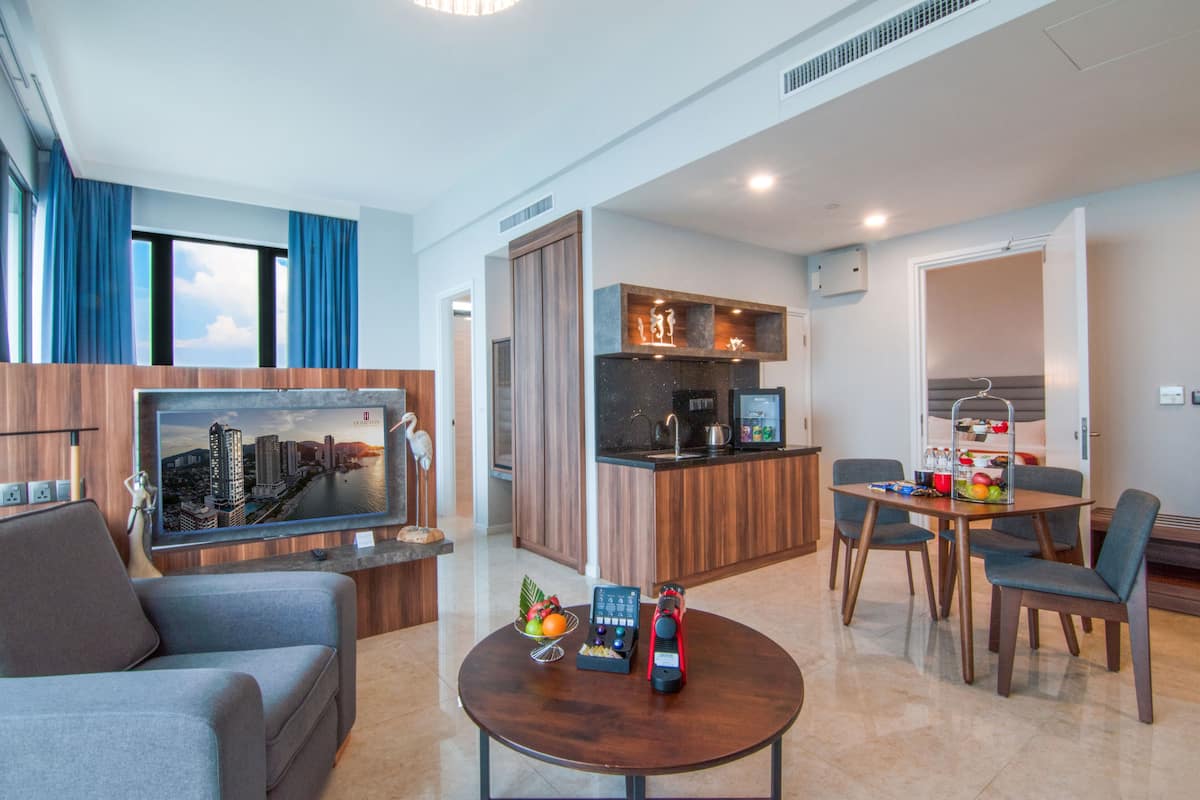 A modern hotel room with a living area, a kitchen, and a dining space.