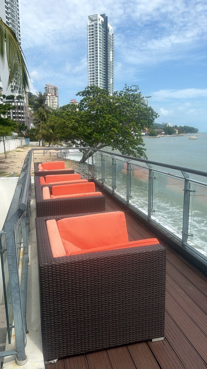 Un paseo marítimo con sillones de mimbre y una barandilla con vistas al mar.