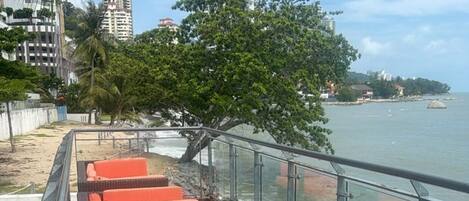 A waterfront promenade with wicker lounge chairs and a railing overlooking the sea.