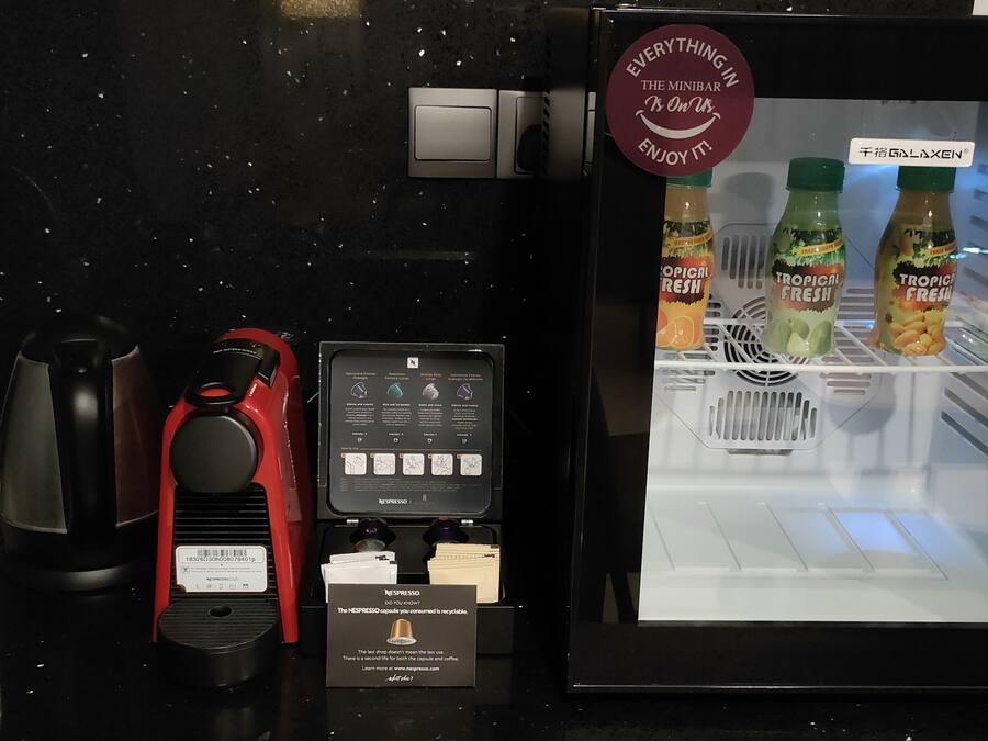 A minibar with a refrigerator containing beverages, a coffee machine, and a water dispenser.