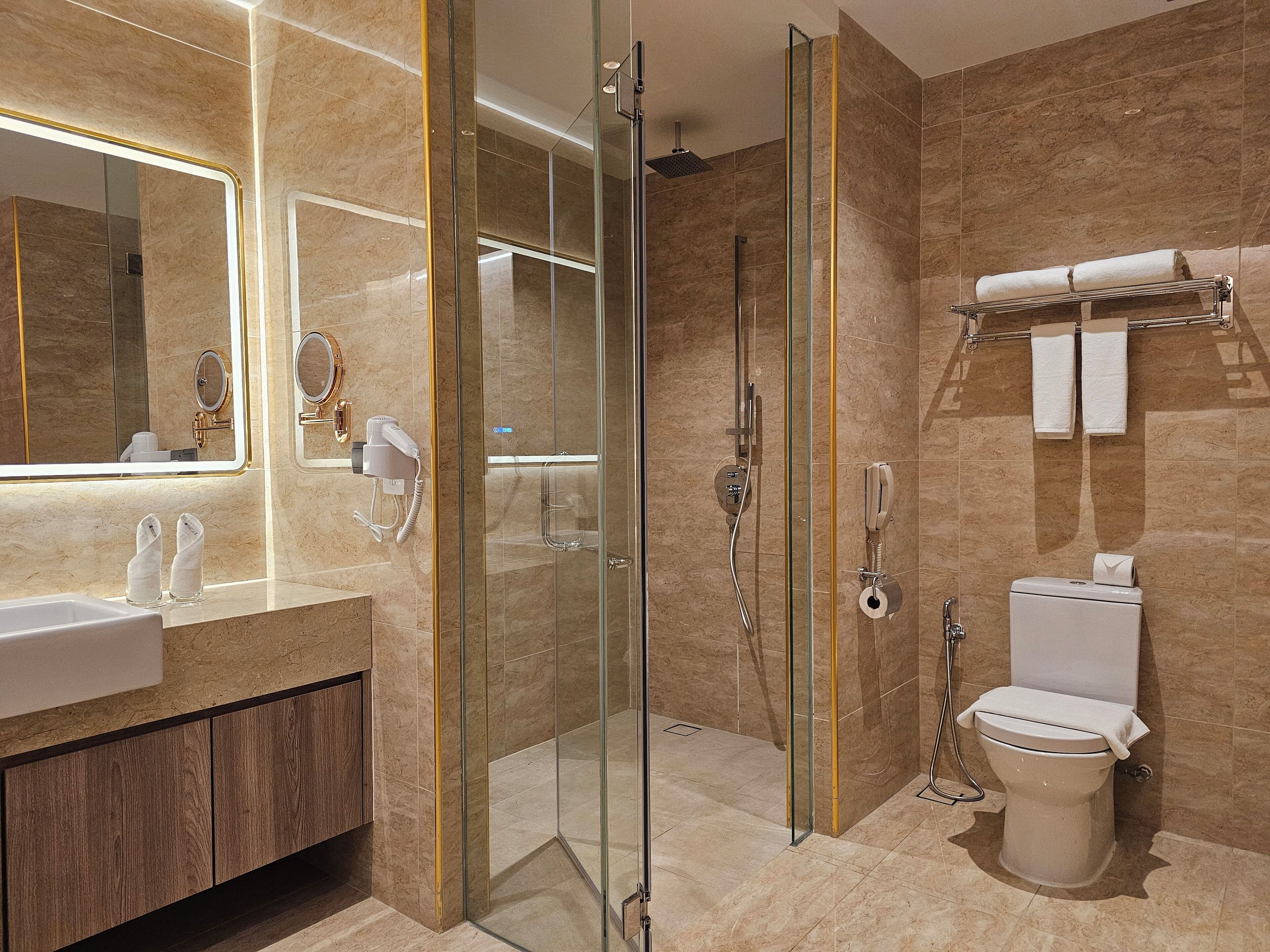 Une salle de bain moderne avec une douche à parois de verre, des toilettes dotées d’un porte-serviettes en papier et un meuble-lavabo avec un miroir et un sèche-cheveux.