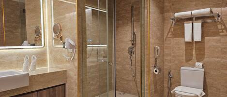 A modern bathroom with a glass-enclosed shower, a toilet with a paper towel holder, and a vanity with a mirror and a hairdryer.