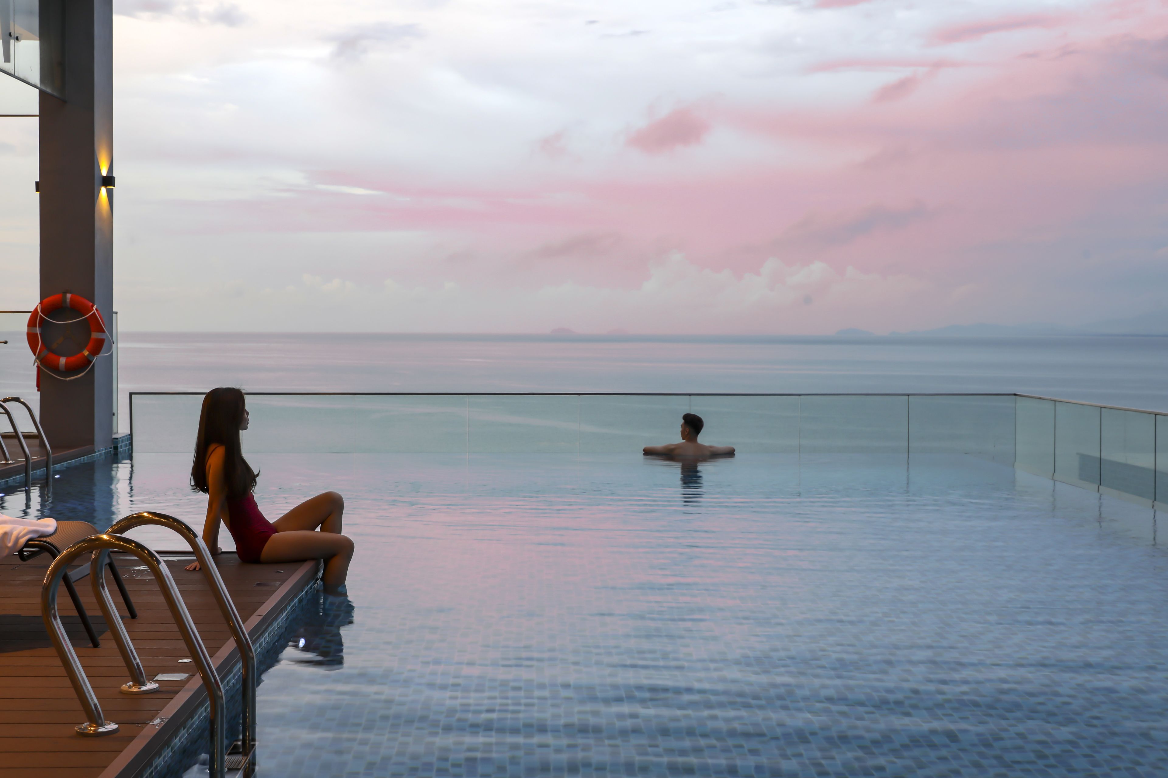 A pool with a view of the sea, a lifebuoy, and a person swimming.