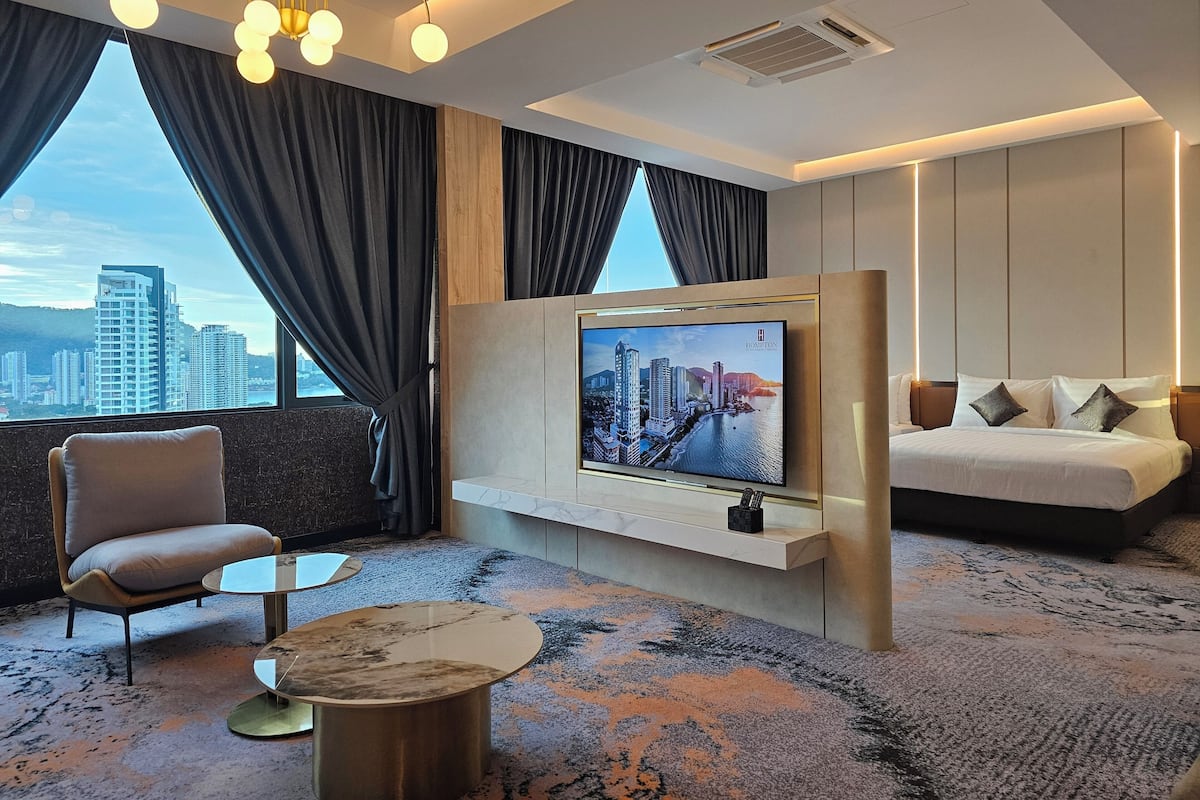 A modern hotel room with a large TV mounted on the wall, a comfortable sofa, a chair, and a coffee table.