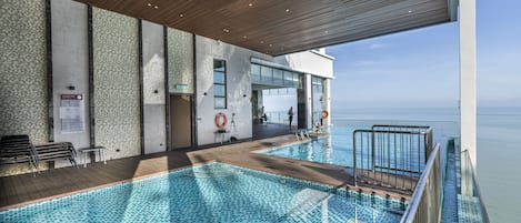 Piscina interior moderna con vista al mar, terraza de madera y zona cerrada con vidrio.