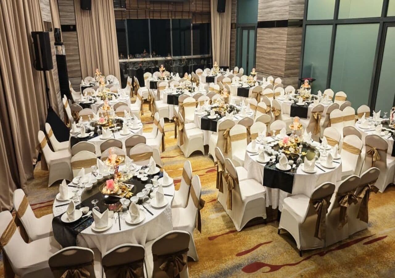 A banquet hall with round tables, white chairs, and black tablecloths.