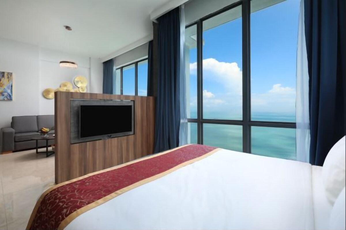 A hotel room with a large bed, a flat-screen TV, a sofa, and a view of the ocean.