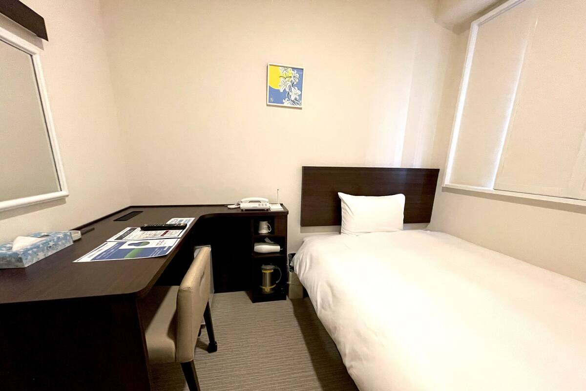 A hotel room with a bed, a desk, a chair, a small table, a telephone, a coffee maker, and a picture on the wall.
