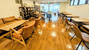 A library with wooden tables and chairs, bookshelves, and a view through large windows. - Hachioji Sky Hotel (Hachioji)