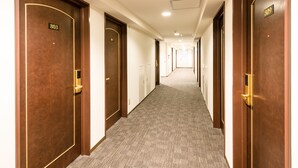 A hotel corridor with wooden doors, carpeted floors, and a modern ceiling design. - Hachioji Sky Hotel (Hachioji)