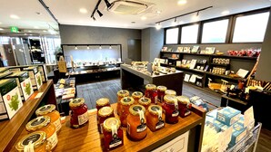 A store interior with shelves of products, a counter with jars, and a display of framed pictures. - Hachioji Sky Hotel (Hachioji)