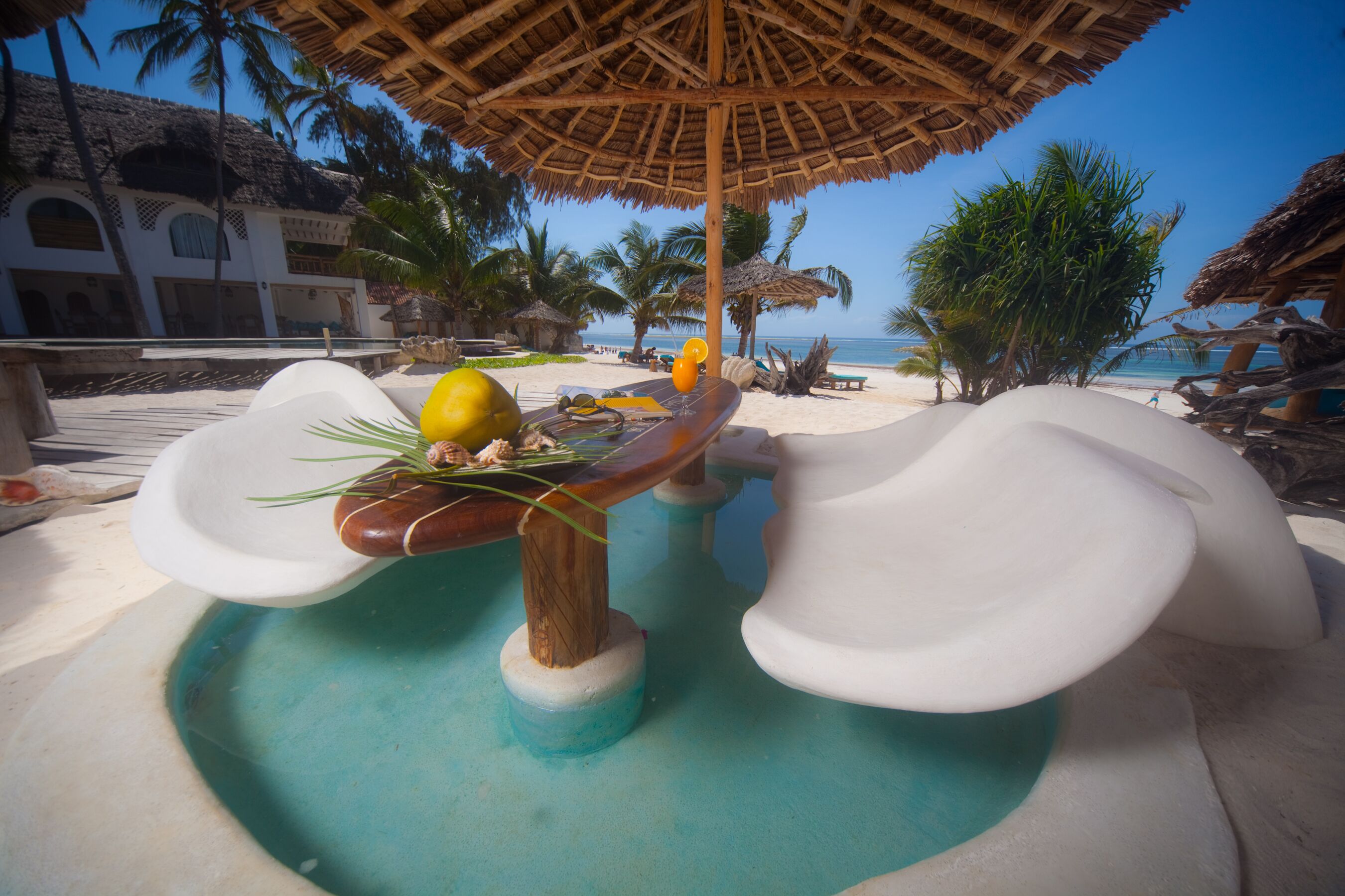A pool area with a wooden bar, a thatched umbrella, and a view of the beach and ocean.