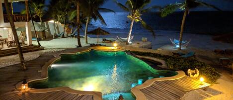 Relax by the infinity pool overlooking the ocean, surrounded by palm trees and a sandy beach.