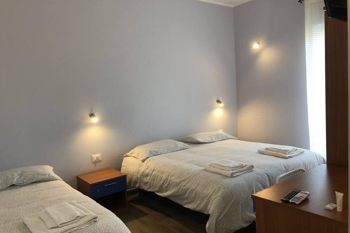 A bedroom with two beds, a wooden nightstand, a small table with a phone and toiletries, and wall-mounted lights.