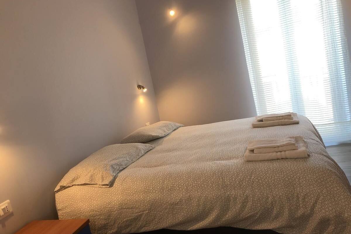A neatly made bed with a patterned bedspread and two folded towels, a bedside table, and a wall-mounted light fixture.