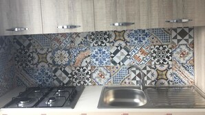 A kitchen with a gas stove, a sink, and a backsplash with colorful tiles. - Profumo di Zagara (Corigliano-Rossano)