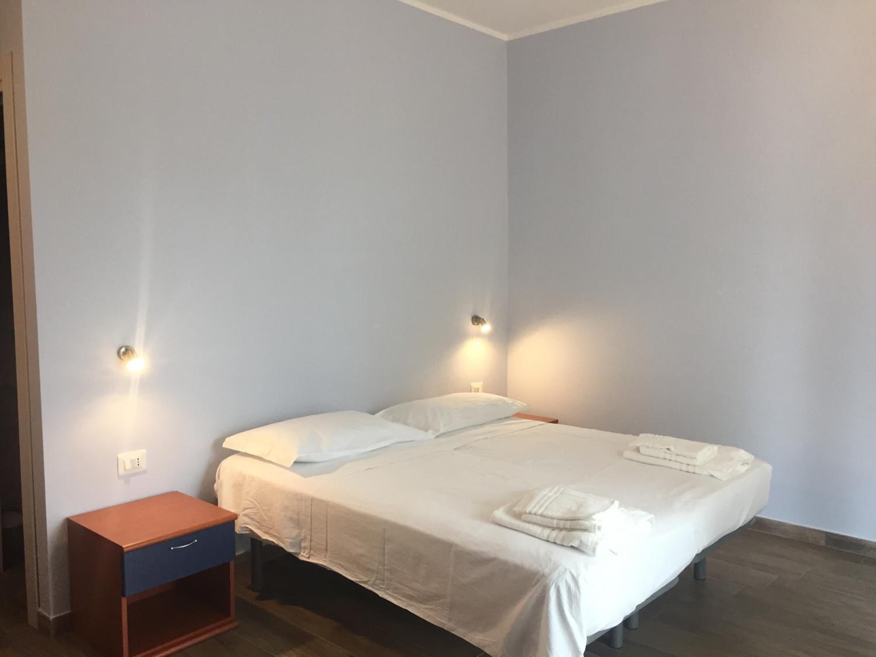 A bedroom with a single bed, bedside tables, and wall-mounted lights.