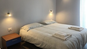 A neatly made bed with a patterned bedspread and pillows, a small wooden nightstand with a drawer, and two wall-mounted lights. - Profumo di Zagara (Corigliano-Rossano)