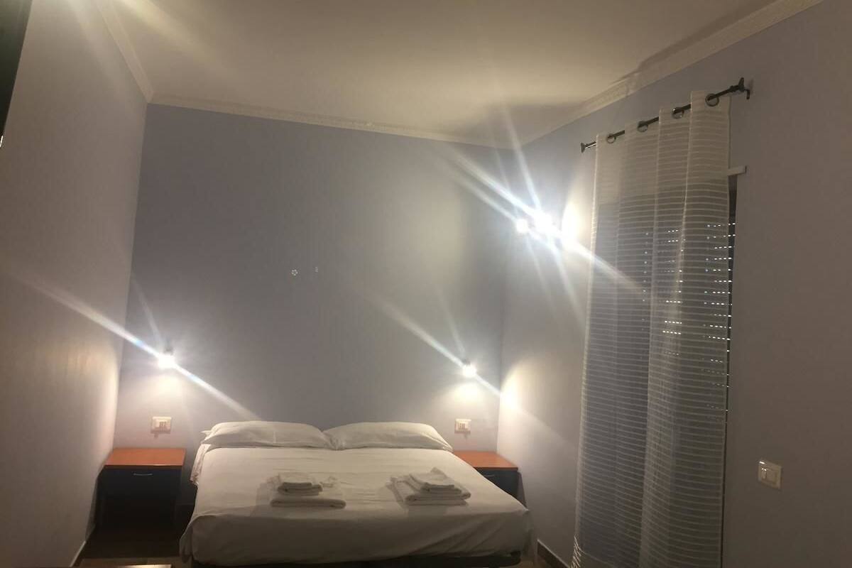 A bedroom with a bed, two bedside lamps, a window with blinds, and a nightstand.