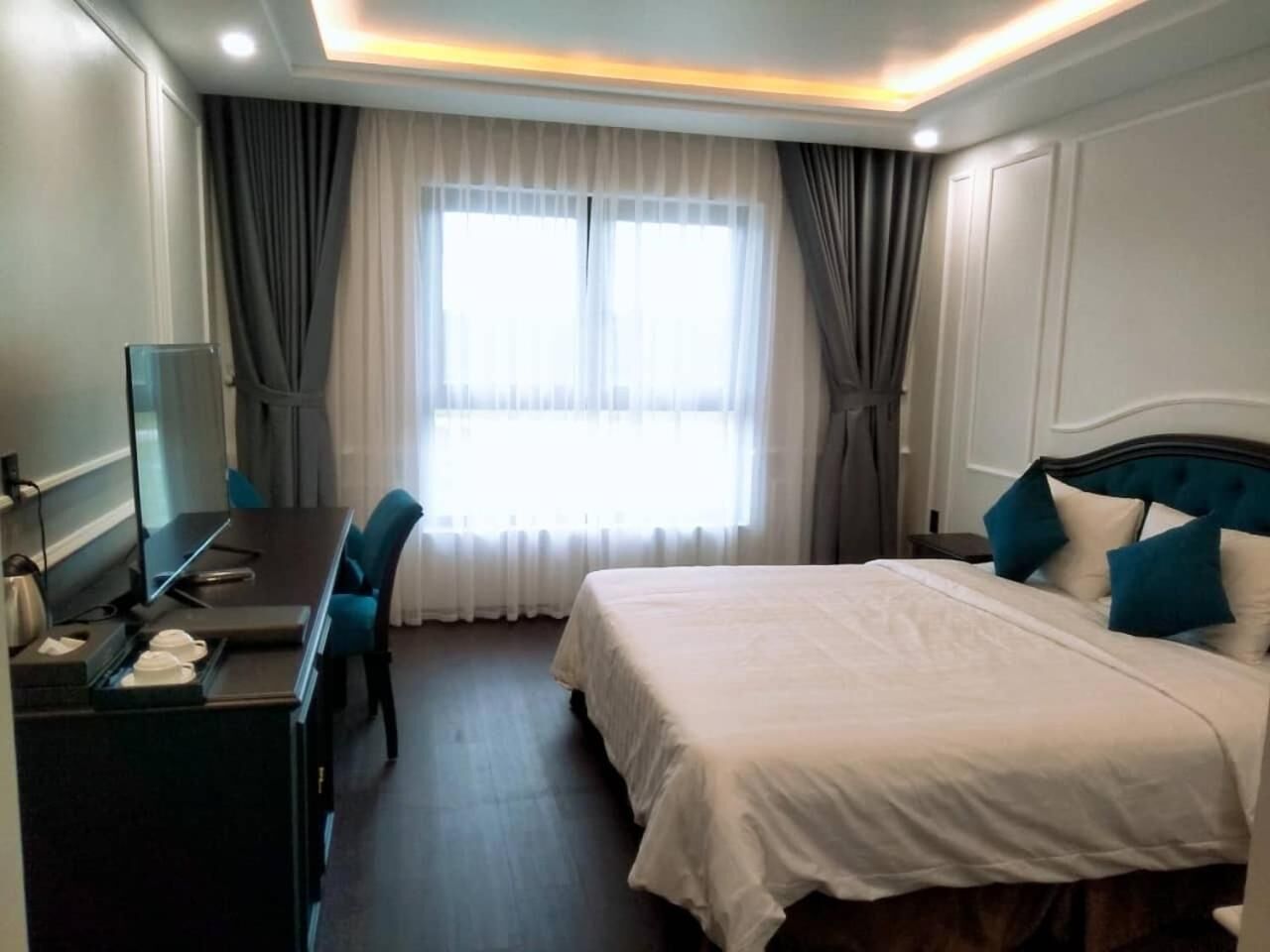 A hotel room with a bed, a desk, and a chair. There is a window with curtains, and the room has a modern design.