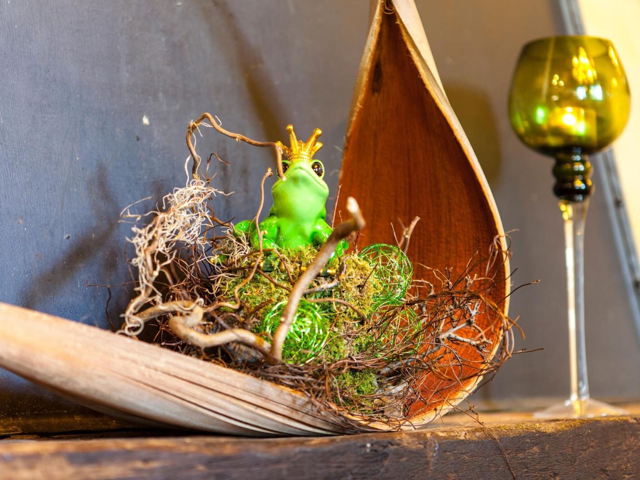 A wooden nesting box with a green frog figurine and a wine glass.