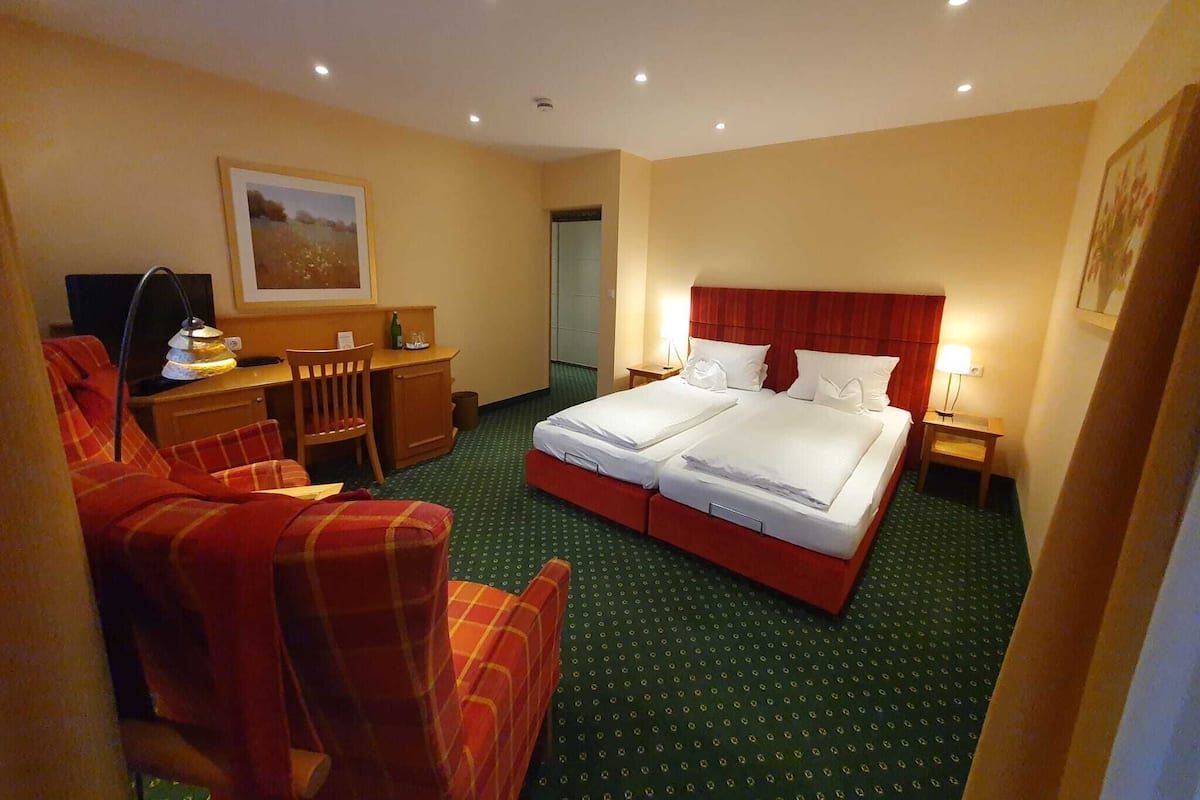 A hotel room with a double bed, a desk with a chair, a television, and a painting on the wall.