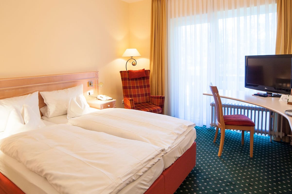 A hotel room with a large bed, a desk with a television, a chair, and a lamp.