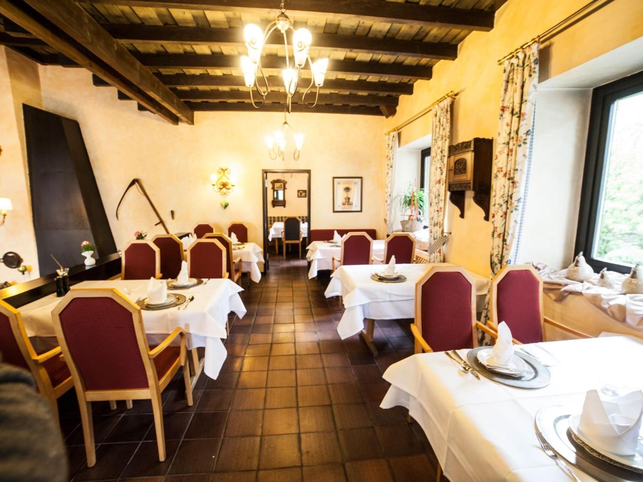 Restaurante com vigas de madeira, toalhas de mesa brancas e cadeiras vermelhas.