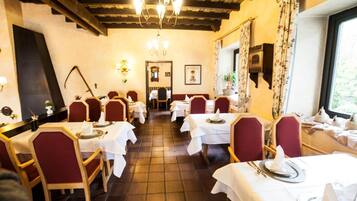 Restaurante com vigas de madeira, toalhas de mesa brancas e cadeiras vermelhas.