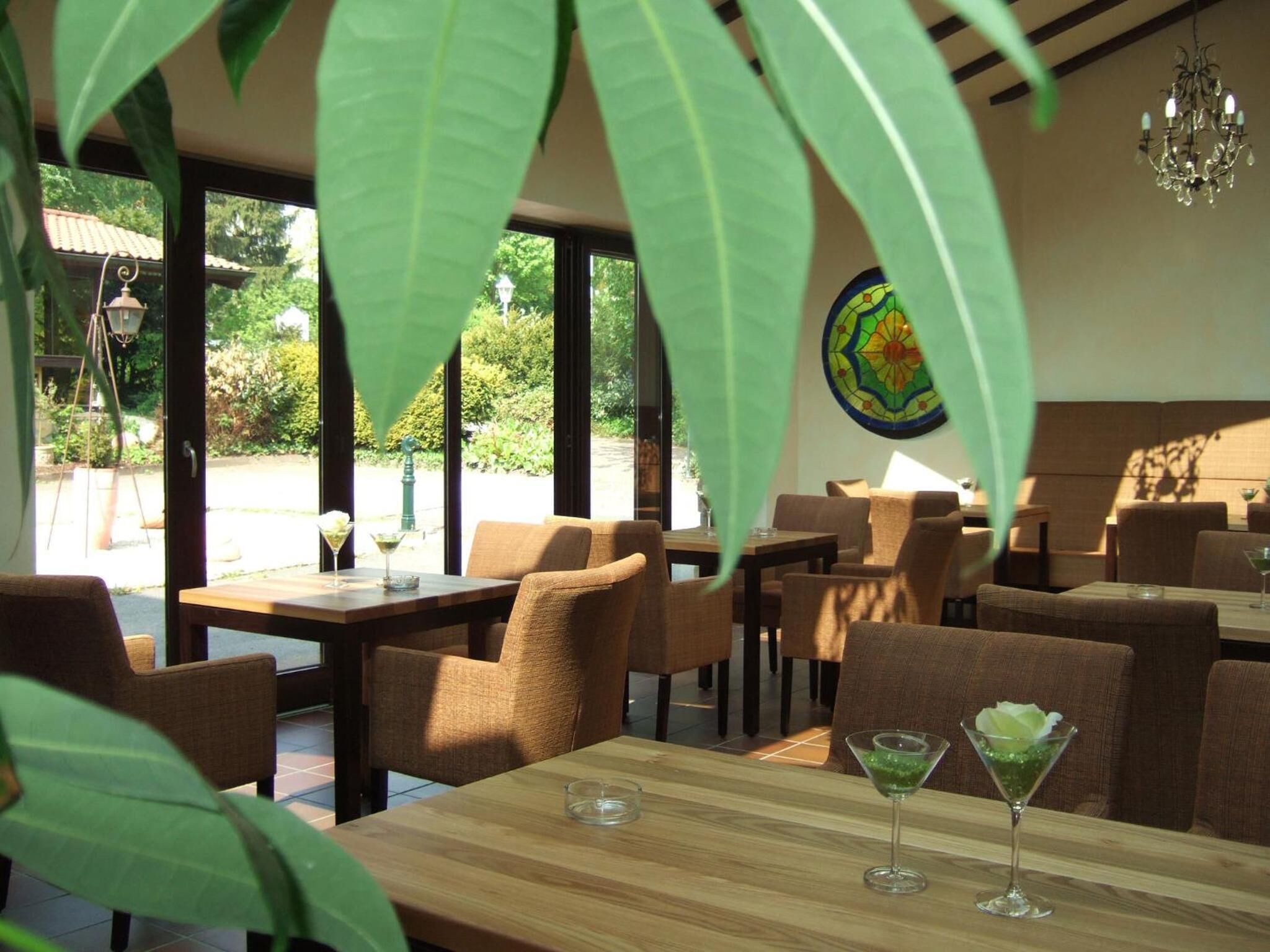 Comedor interior con mesas de madera y sillas acolchadas, ventanas amplias y un candelabro.