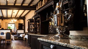 L’intérieur d’un restaurant est orné de boiseries sombres, et on y trouve une grande théière en argent ouvragée, ainsi qu’un coin repas chaleureux avec des tables et des chaises.