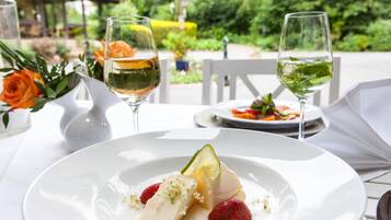 Una mesa dispuesta para una comida, con un plato de postre, dos copas de vino blanco y un jarrón con flores.