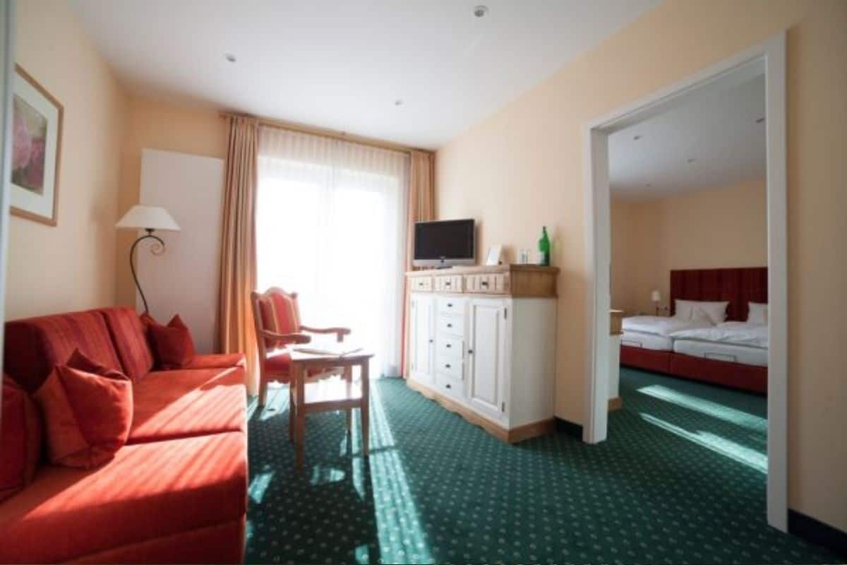 A hotel room with a red sofa, a desk, a TV, and a wardrobe.